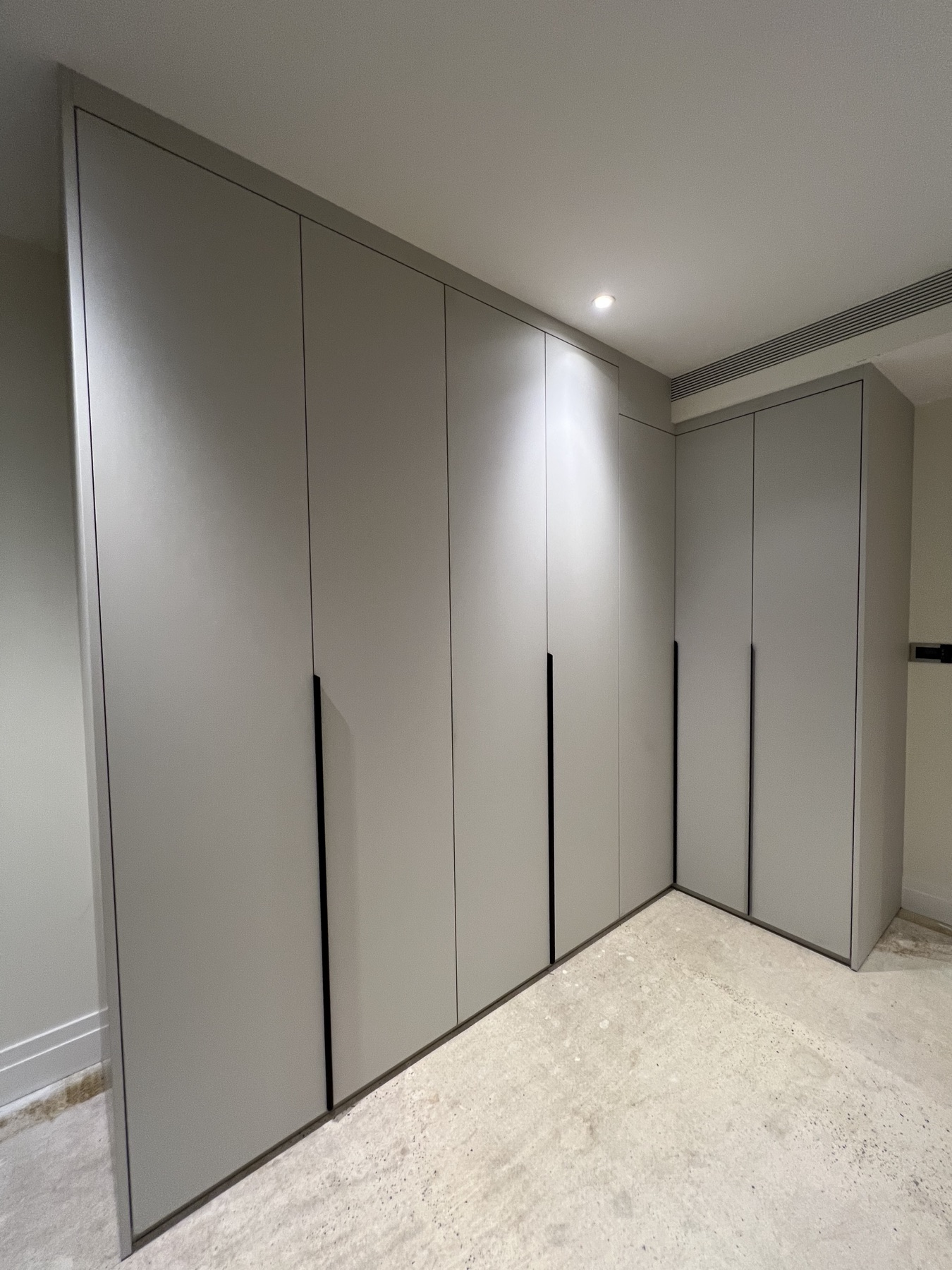 Completed floor-to-ceiling fitted wardrobes with flush grey doors and black handles