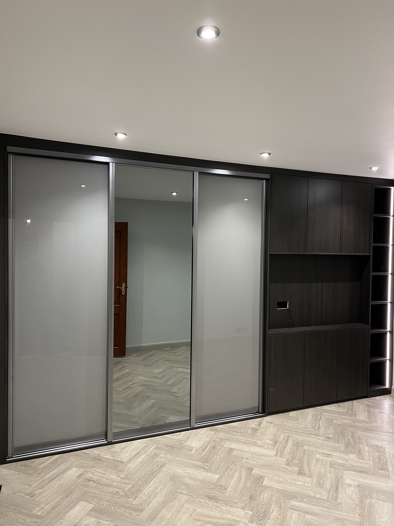 Completed sliding wardrobe wall with integrated cabinetry and illuminated display shelving