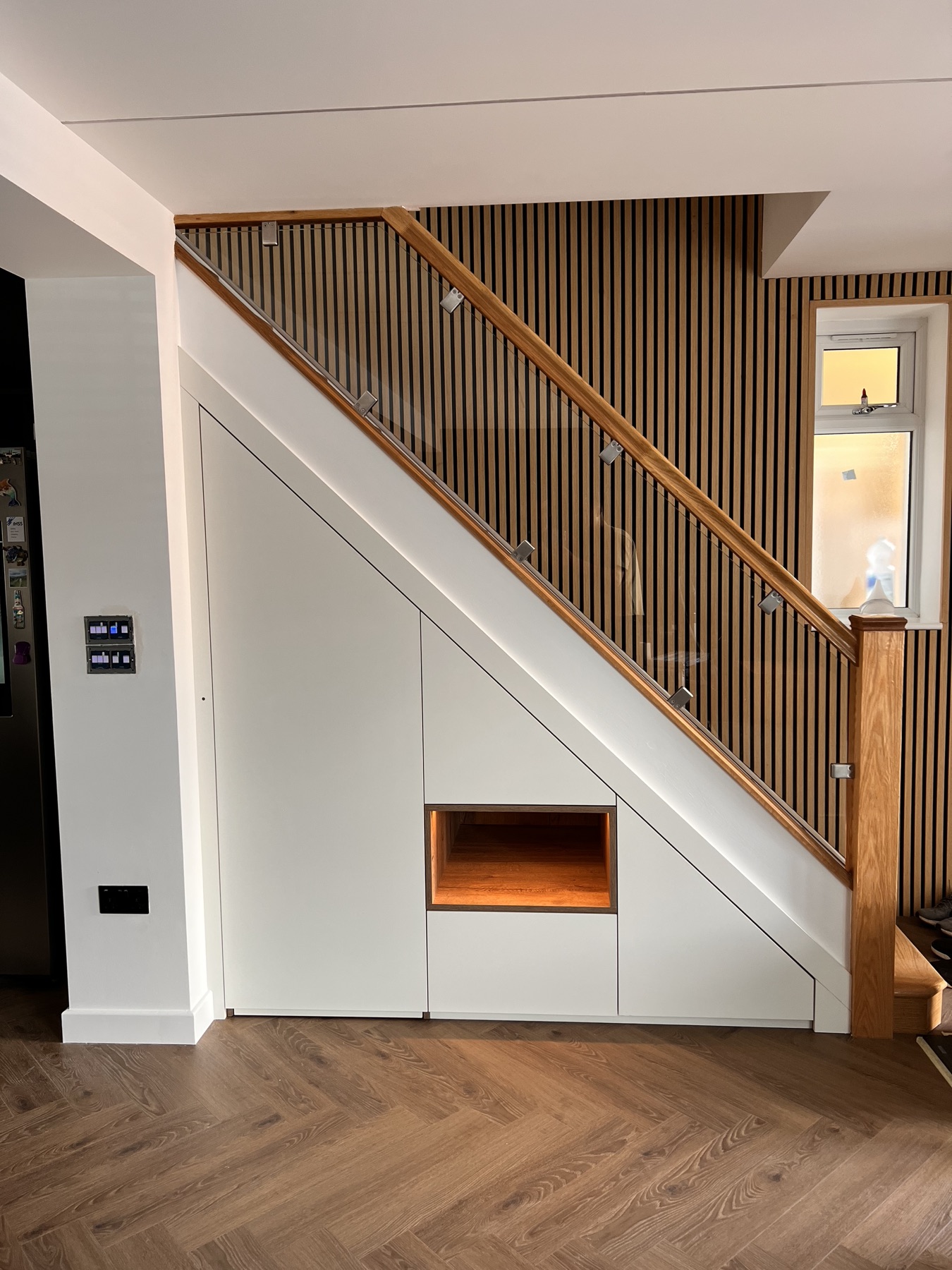 Completed made-to-measure understairs cabinetry with concealed doors and illuminated display niche